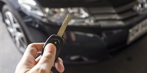 Man hold car remote key for unlock or lock the black car in background.